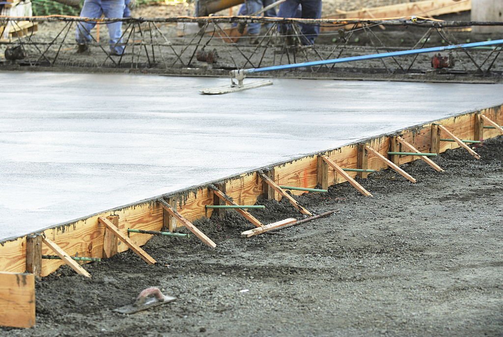 Masonry construction workers smooth freshly poured concrete using bullfloat tool.