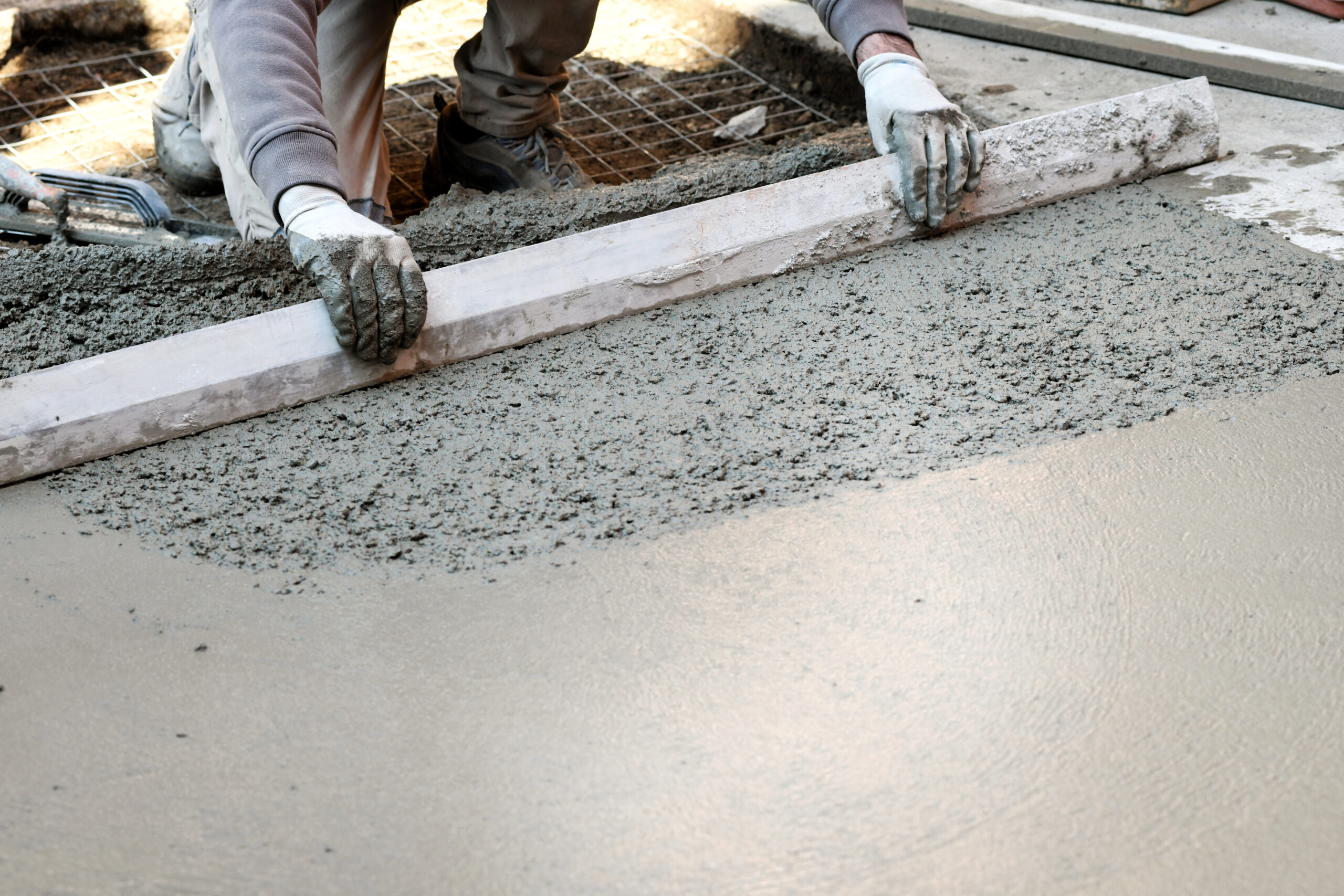 Worker spreading and flattening cement mortar with hand tool, making concrete floor